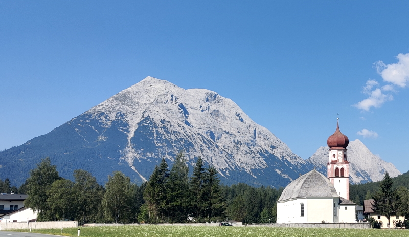 St Magdalena Church from the 12 century on the outskirts of Wiedach in Leutash, with Alpine peaks behind. As seen from the Adlerweg route with Alpine Exploratory.