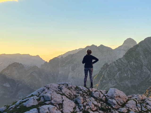 Hiker silhouetted by the sunset outside Koča na Doliču